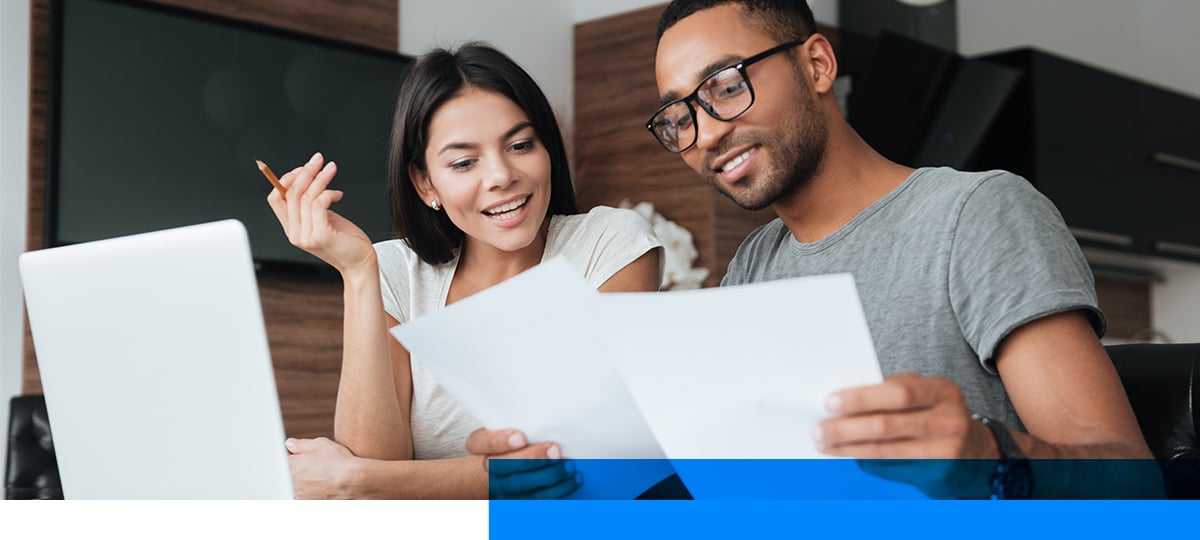 Young couple reviewing laptop and paperwork.