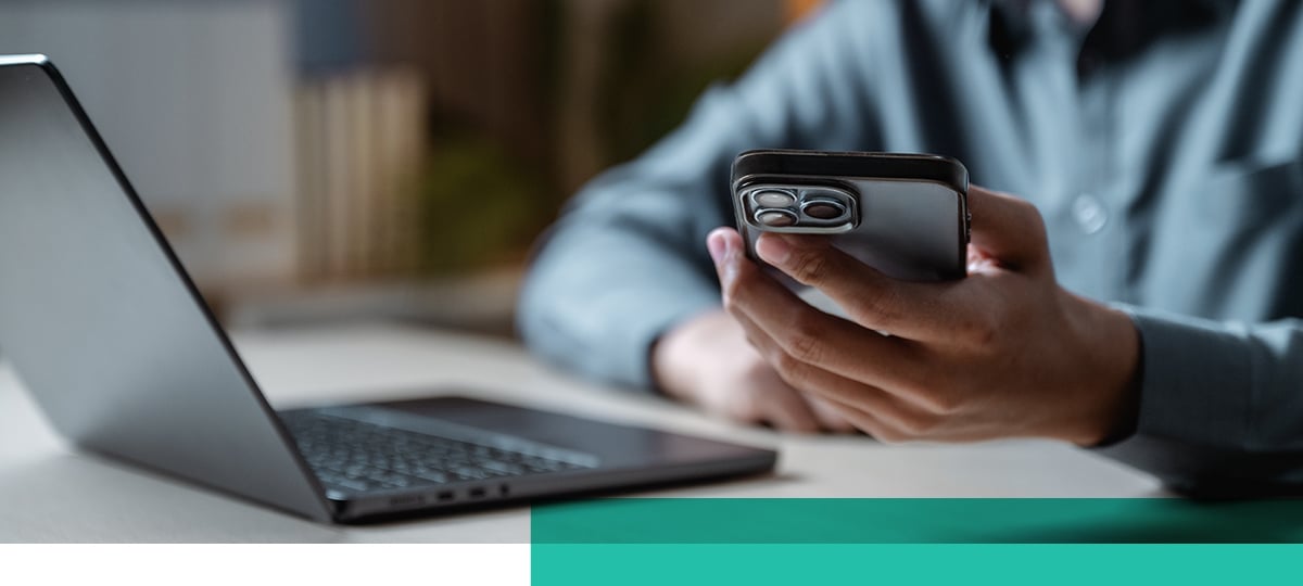 Closeup of a person holding their phone in front of a laptop.